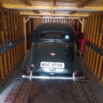 A black vintage car loaded onto a carrier for vehicle transportation service in Bangalore.