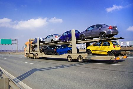 A yellow truck loaded with cars travels along a highway, showcasing the car transport process in India.